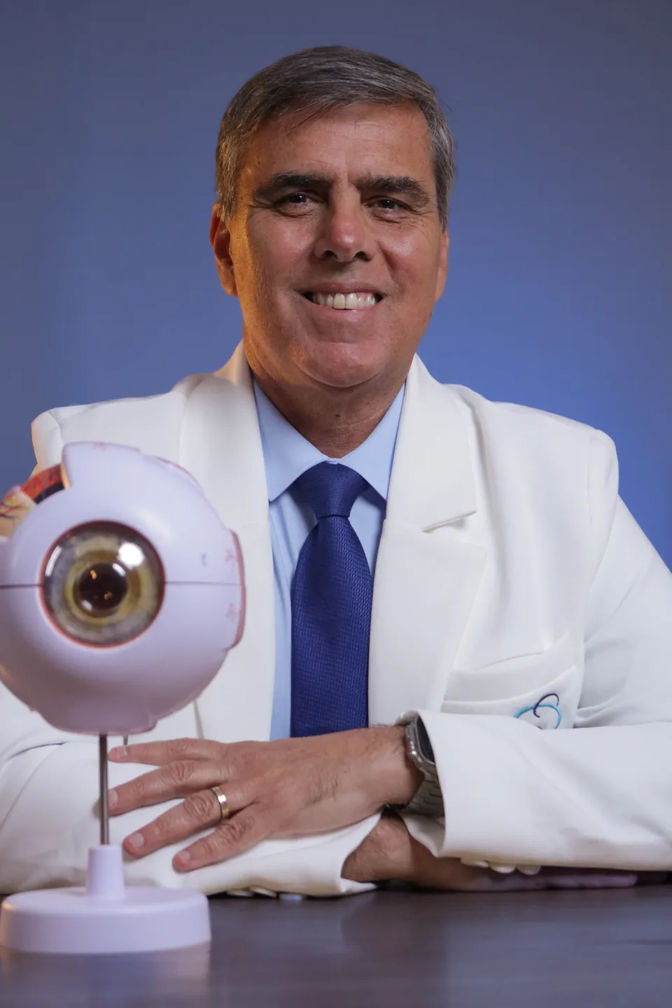 Dr. Durval Valença Filho, de jaleco, ao lado de um modelo anatômico do olho